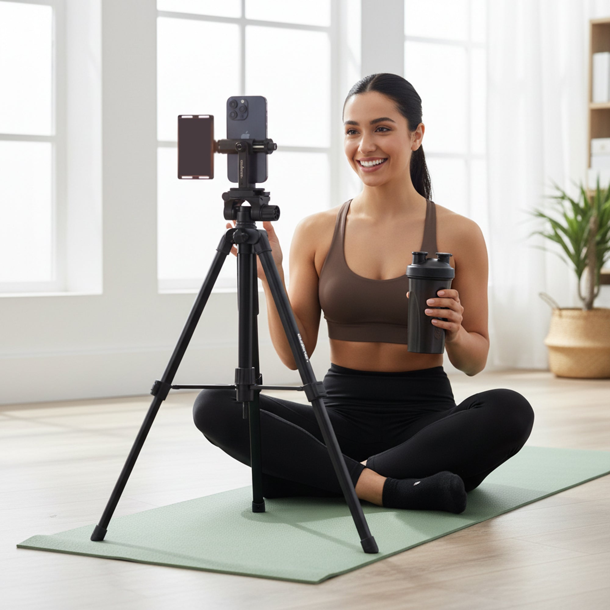 Woman on a yoga mat with a camera on a tripod and a shaker bottle.